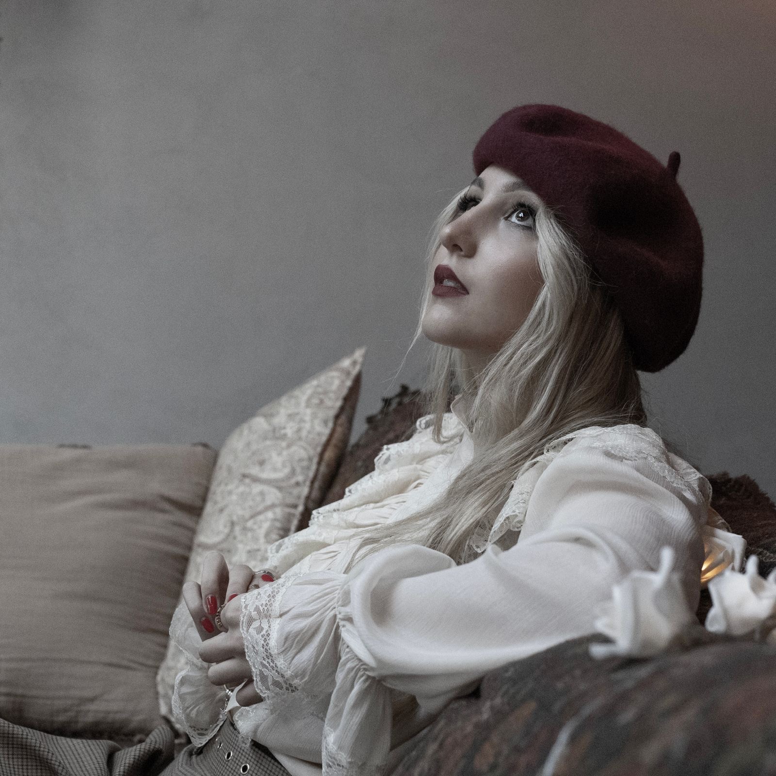Carolina Quintas, cantora, em retrato editorial com boina bordeaux e blusa de renda branca